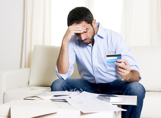 stressed man holding credit card and looking at bills