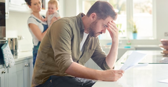 man looking at financial documents with wife and baby in background