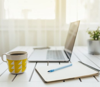 work table with a laptop, notepad, and a cup of coffee